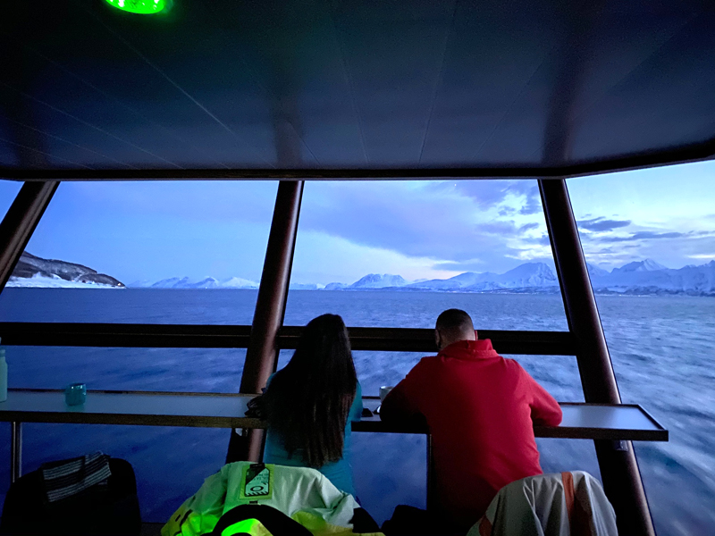 "planet e.: Verändert grünes Geld die Welt?": Eine Frau und ein Mann, mit dem Rücken zur Kamera, sitzen an einem Panoramafenster auf einem Ausflugsboot und blicken aufs Wasser.