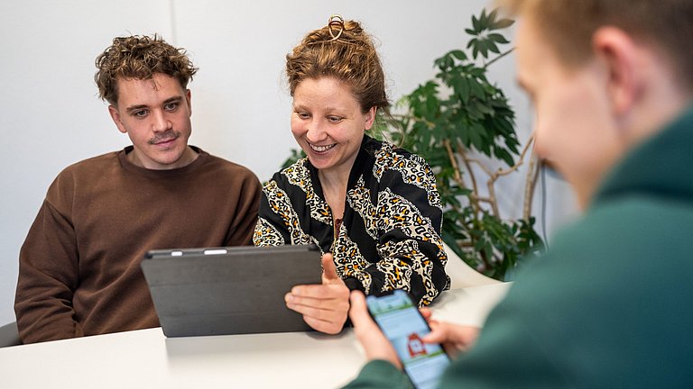 Drei Personen tauschen sich über Arbeitsmaterialien aus.
