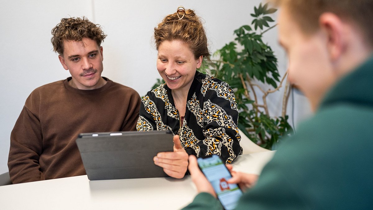 Drei Personen tauschen sich über Arbeitsmaterialien aus.