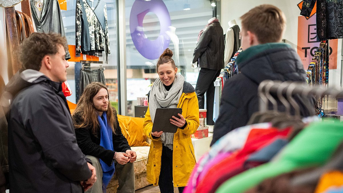 Sabrina steht mit einer Gruppe Menschen im Second Hand Laden. 