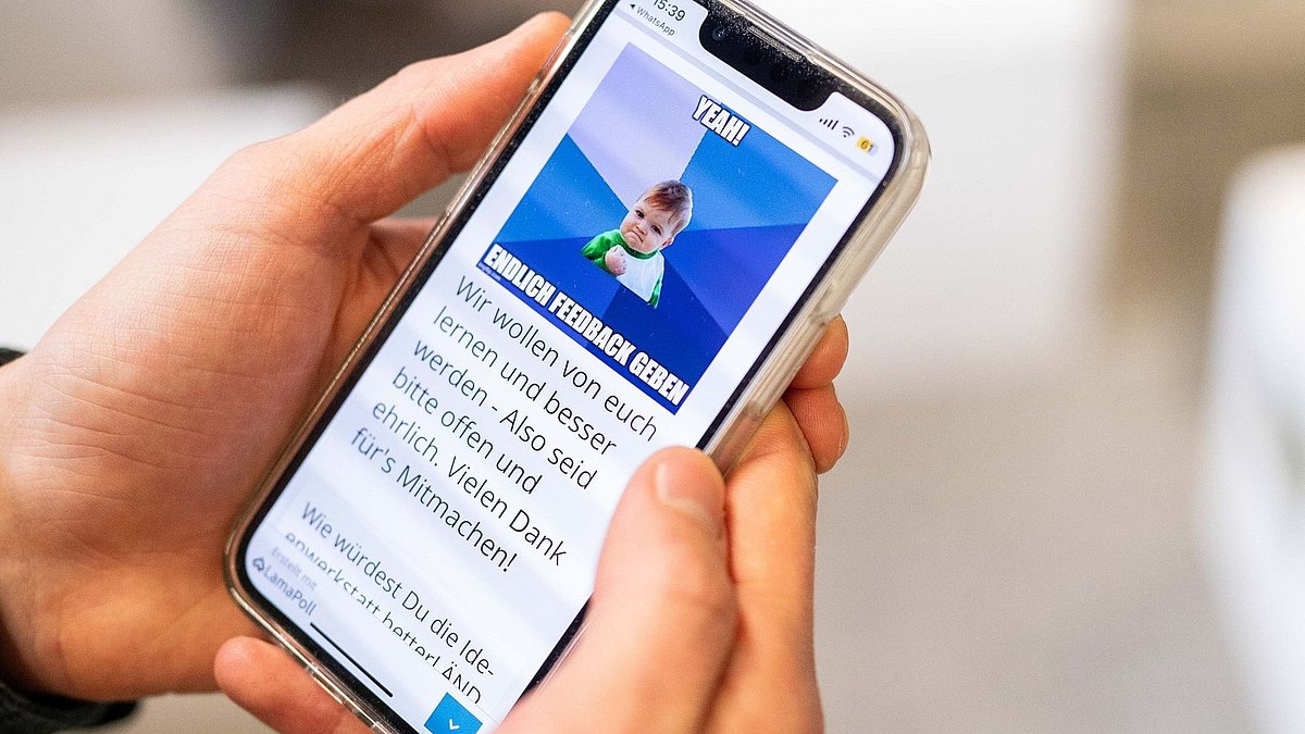 Ein Handy wird von zwei Händen gehalten, auf dem Bildschirm ist eine Feedback-Abfrage zu sehen.