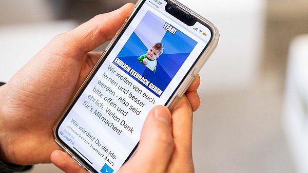 Ein Handy wird von zwei Händen gehalten, auf dem Bildschirm ist eine Feedback-Abfrage zu sehen.