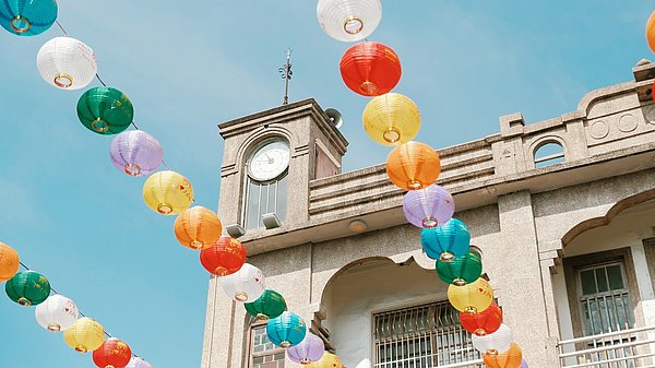 Bunte Lampions hängen in der Luft, im Hintergrund ein Gebäude