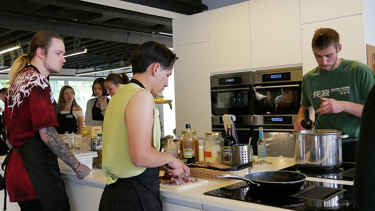 Menschen in einem Kochkurs stehen um eine Kochinsel