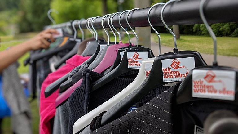 Kleider hängen auf einer Stange mit Logo von WEWWS