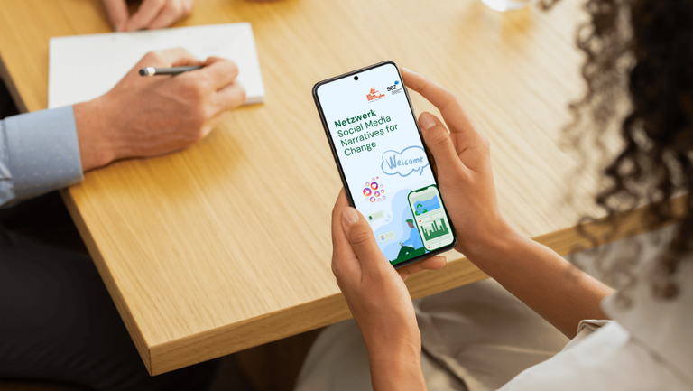 Frau hält Smartphone in der Hand, auf Bildschirm ist das Titelbild des Social Media Netzwerks zu sehen