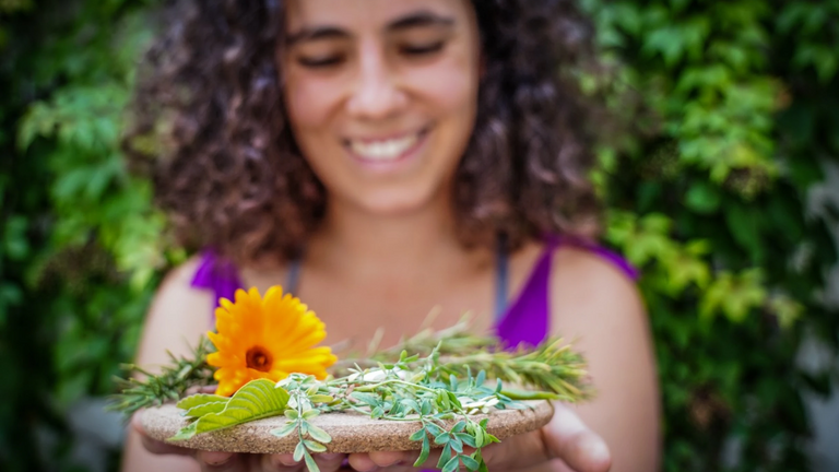 Eine Frau häkt lächelnd Blumen in die Kamera.