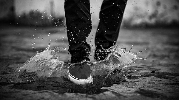 Ein Person steht in einer Pfütze. Es regnet