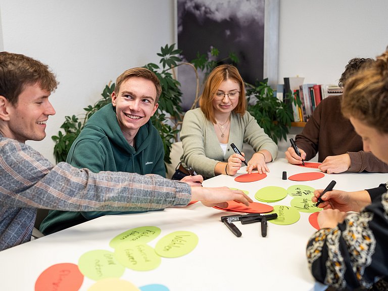 Junge Menschen sitzen an einem Tisch und schreiben auf Moderationskarten. 