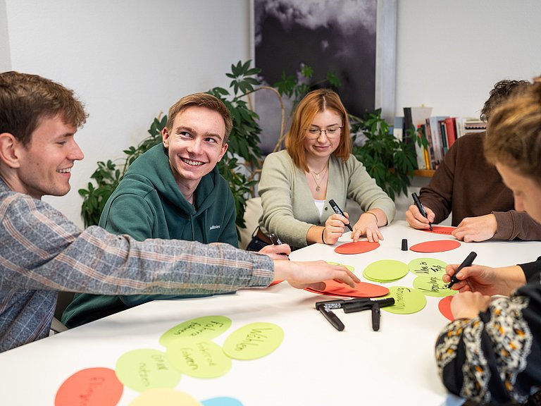 Junge Menschen sitzen an einem Tisch und schreiben auf Moderationskarten. 