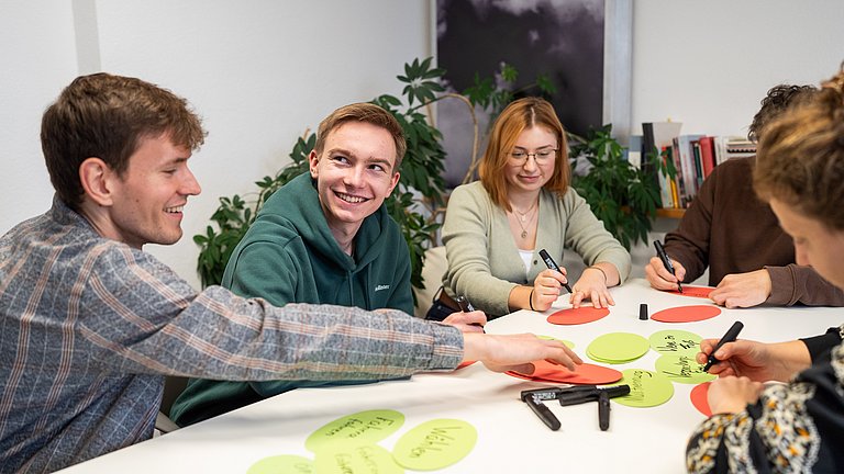 Junge Menschen sitzen an einem Tisch und schreiben auf Moderationskarten. 