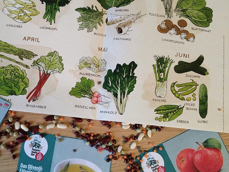 Ein Saisonkalender liegt auf einem Tisch, umgeben von Bohnen und verschiedenen anderen Samen.