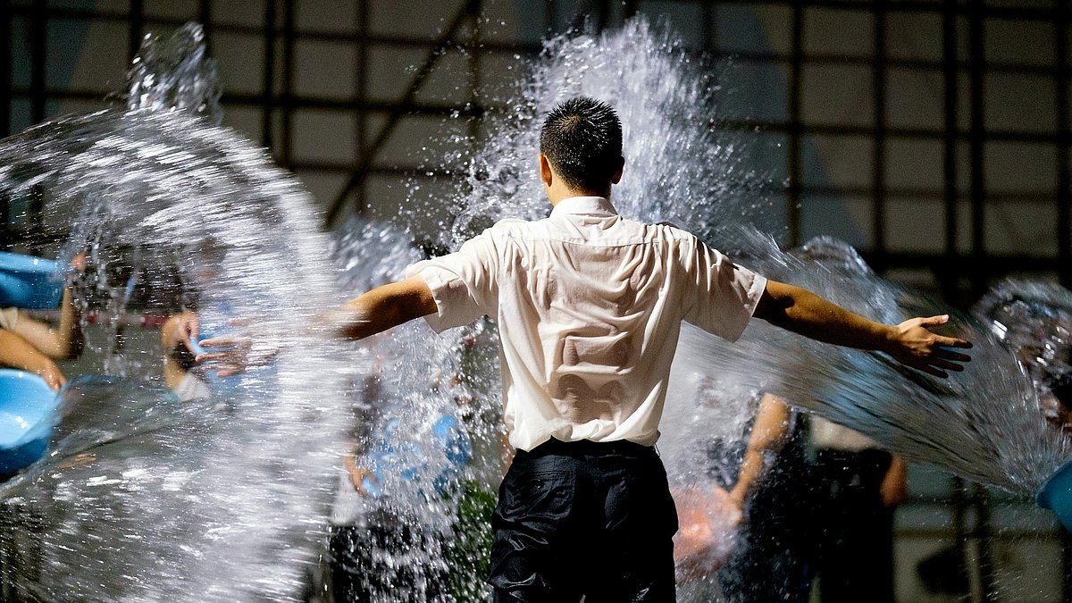 Ein Mann wird mit Wasser aus mehreren Eimern von der Seite nass gespritzt
