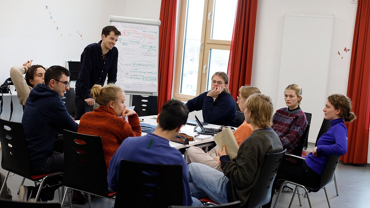 Arbeitsgruppe sitzt am Tisch, eine Person steht und referiert