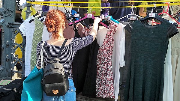Eine junge Frau schaut sich gebrauchte Kleidungsstücke an, die an Bügeln hängen.