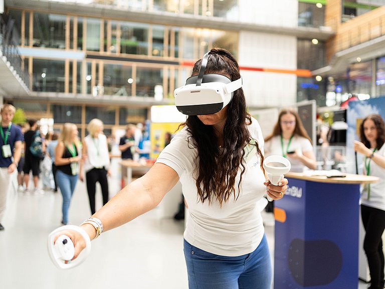 Junge Frau mit VR Brille und Steuerlement in der Hand steht dynamisch im Raum