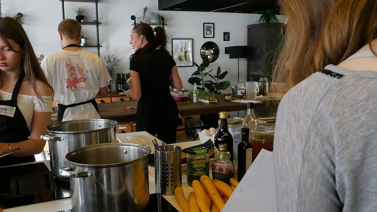 Menschen in einem Kochkurs stehen um eine Kochinsel
