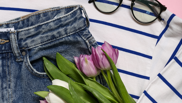 Eine Jeans in deren Tasche Tulpen stecken, ein weißes Shirt und eine Brille.