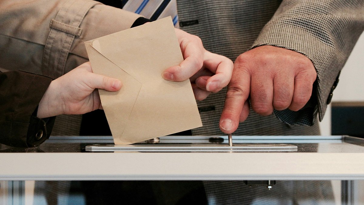 Mehrere Hände werfen Wahlumschläge in eine Wahlurne ein