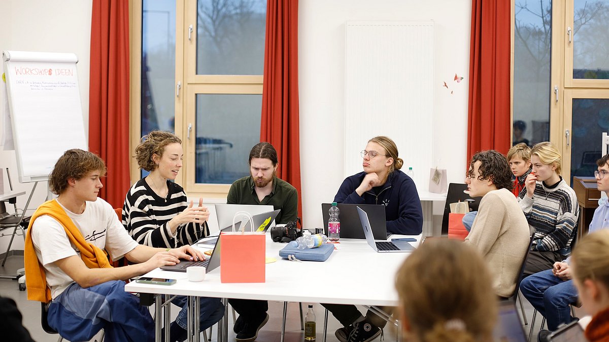 Arbeitsgruppe sitzt an Gruppentisch vor Laptops