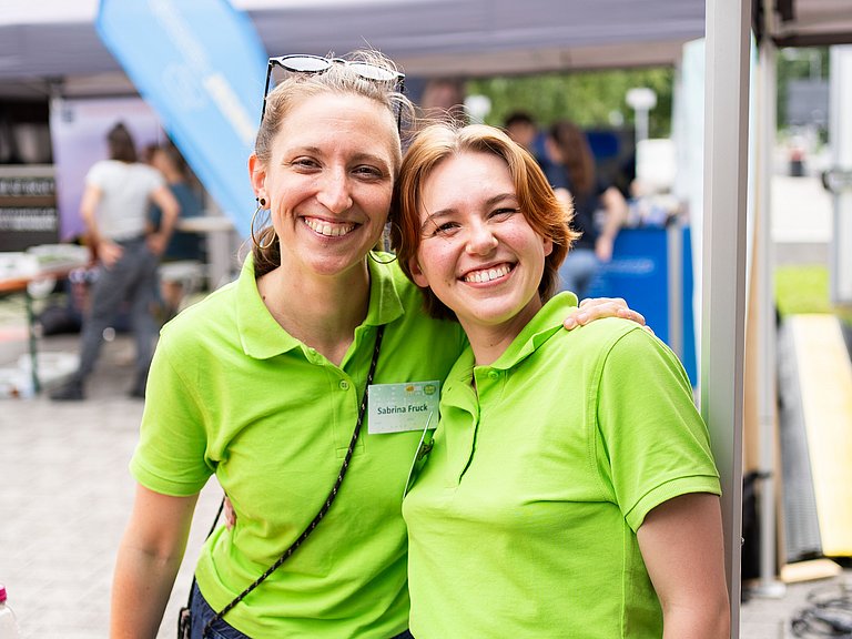 Zwei sympathische junge Frauen die sich den Arm über die Schulter legen und lachen