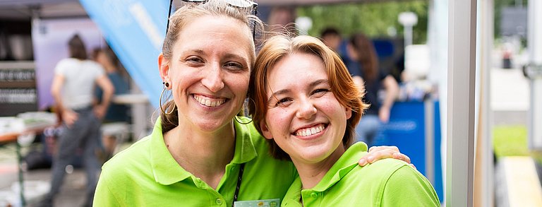 Zwei sympathische junge Frauen die sich den Arm über die Schulter legen und lachen