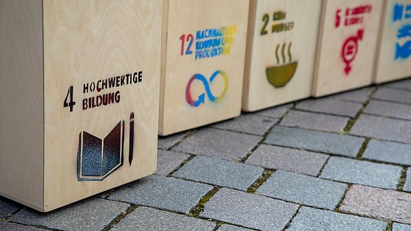 Holzaufsteller mit aufgedruckten SDGs stehen auf dem Boden 
