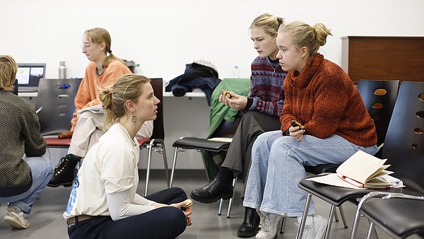 Eine Kleingruppe unterhält sich auf Stühlen, teilweise auf dem Boden sitzend