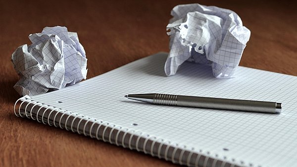 Ein Schreibblock auf einem Tisch mit Stift und zwei zerknüllten Papierseiten