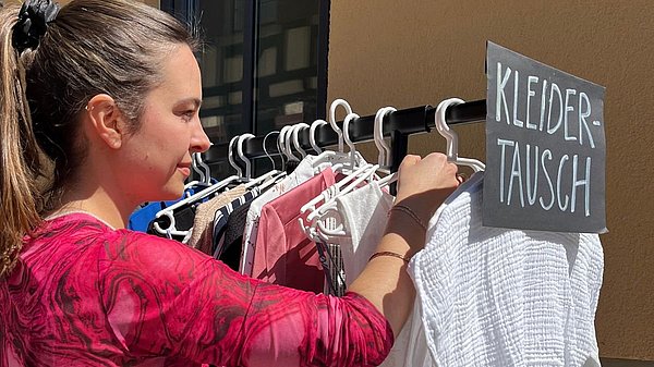 Junge Frau sucht bei Kleidertauschparty an einer Kleiderstange nach Kleidungsstücken.
