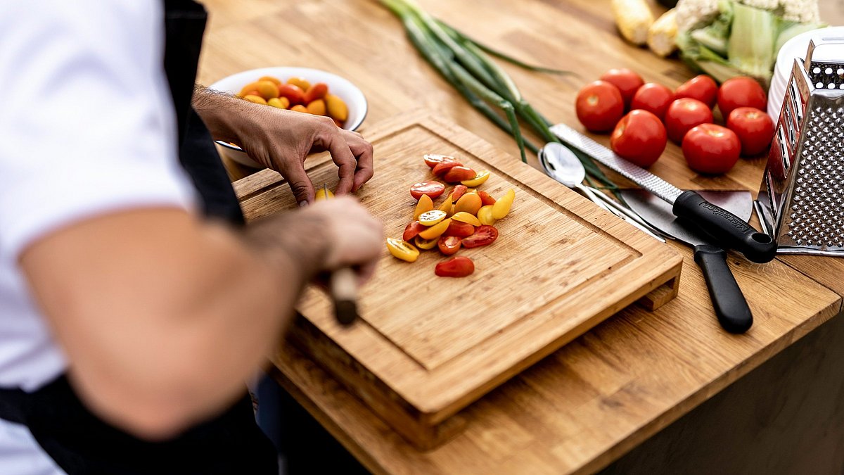 Eine Person schnibbelt auf einem Holzbrett Gemüse klein