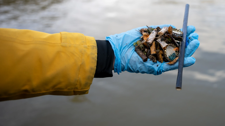 Eine Hand, die Müll aus einem Fluss sammelt.