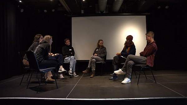 Gruppe sitzt auf Bühne im Kreis und diskutiert