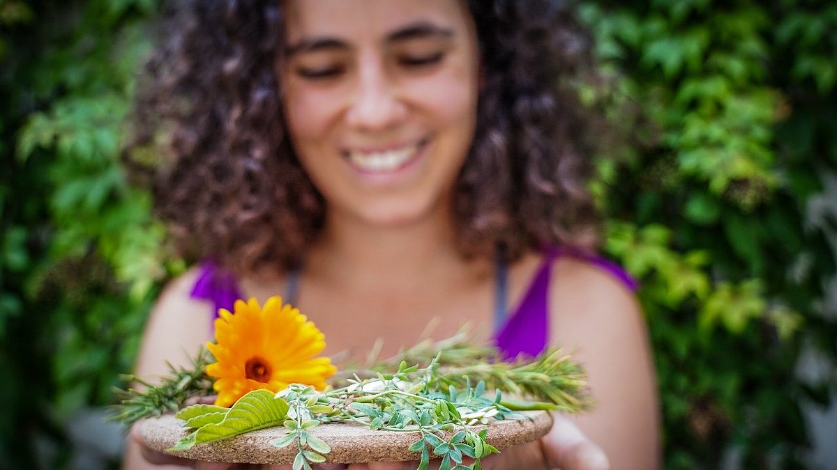 Eine Frau häkt lächelnd Blumen in die Kamera.