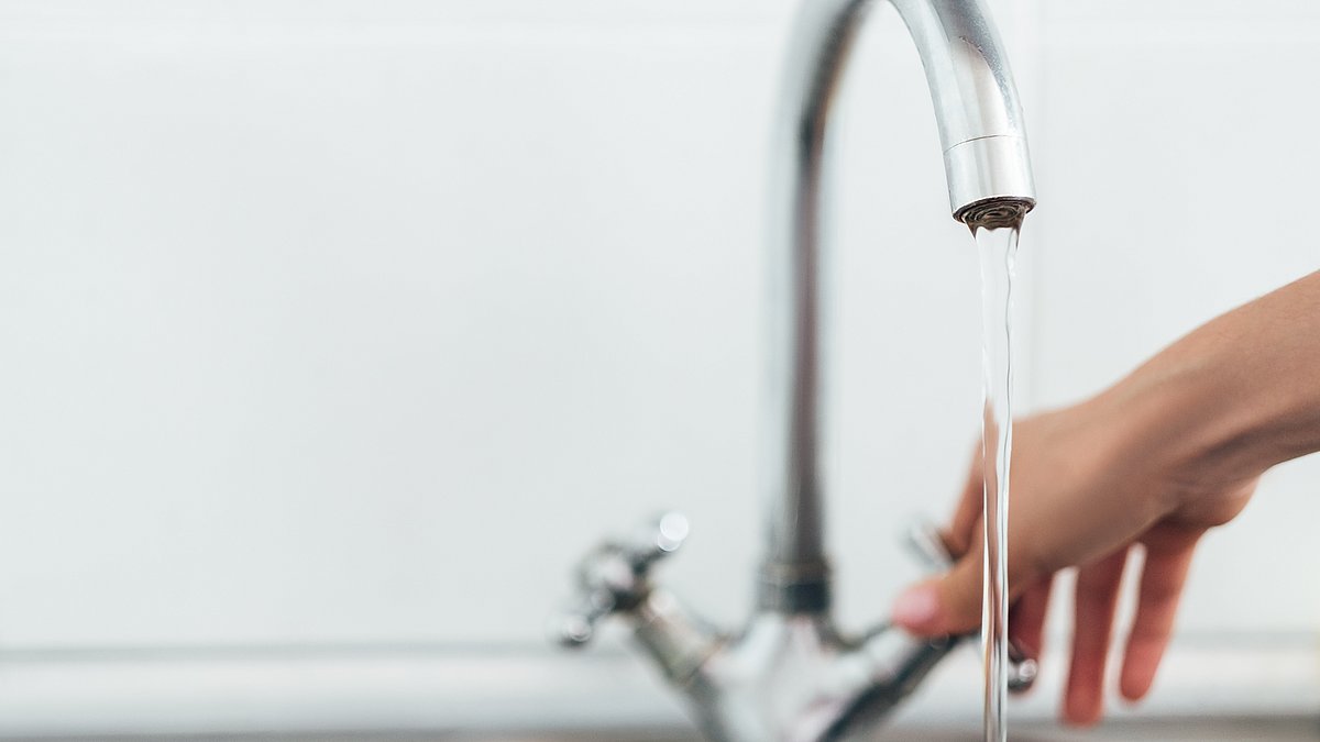 Eine Hand greift zum Wasserhahn und dreht diesen auf. 