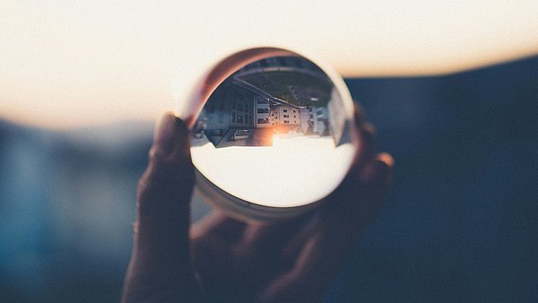 Eine Glaskugel wird in der Hand gehalten, in ihr spiegelt sich eine Häuserfront