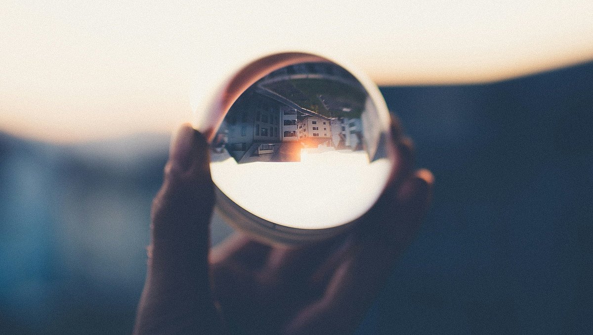 Eine Glaskugel wird in der Hand gehalten, in ihr spiegelt sich eine Häuserfront