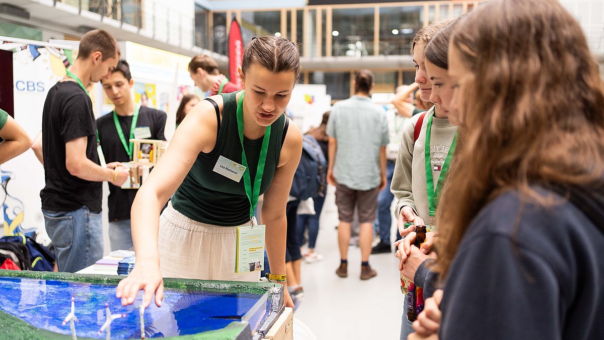Eine Ausstellerin erklärt Jugendlichen ein Windpark-Modell 