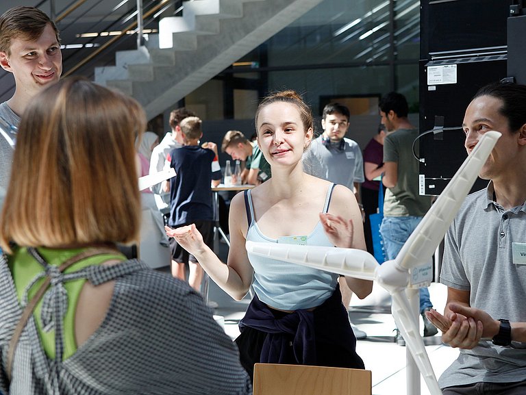 Personen an einem Stand erklären Zuschauenden etwas zu einem Windkraftmodell
