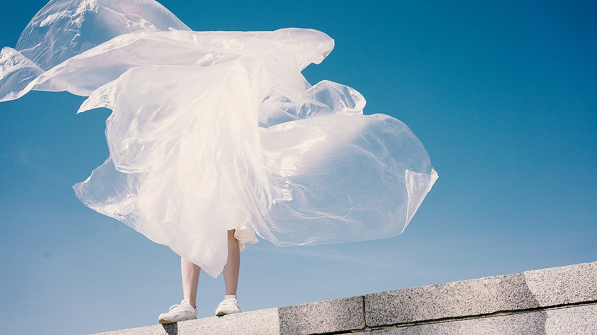 Eine Person trägt eine Plastikverpackung um sich, die im Wind flattert.