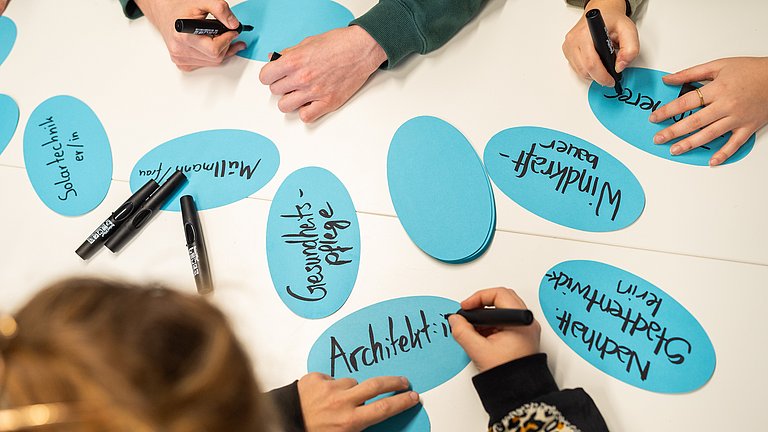 Hände, die grüne Berufe auf Kärtchen schreiben 