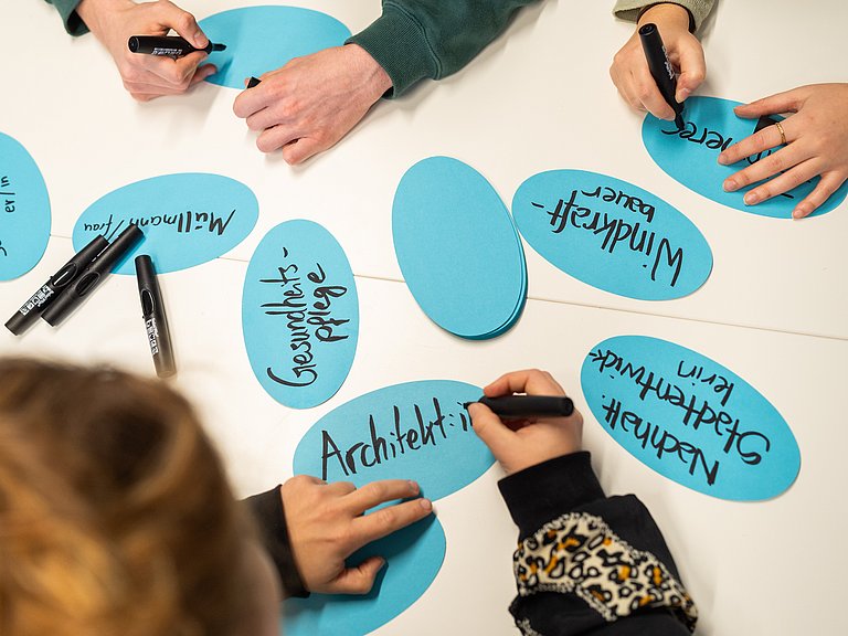 Hände, die grüne Berufe auf Kärtchen schreiben 