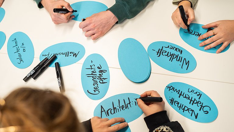 Hände, die grüne Berufe auf Kärtchen schreiben 