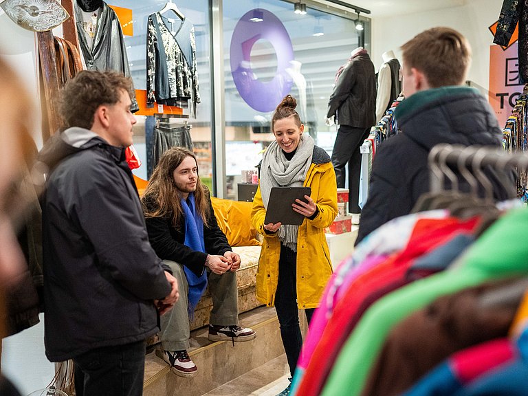 In einem Second Hand Modeladen in Stuttgart erläutert unser Guide Sabrina einer kleiner Gruppe die Vorteile von nachhaltiger Mode.