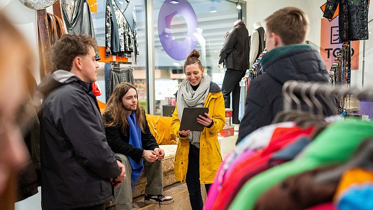 In einem Second Hand Modeladen in Stuttgart erläutert unser Guide Sabrina einer kleiner Gruppe die Vorteile von nachhaltiger Mode.
