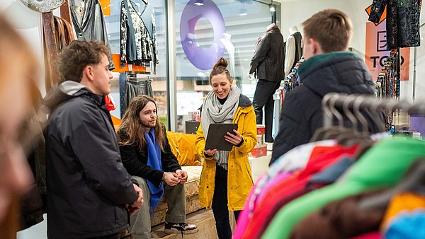In einem Second Hand Modeladen in Stuttgart erläutert unser Guide Sabrina einer kleiner Gruppe die Vorteile von nachhaltiger Mode.