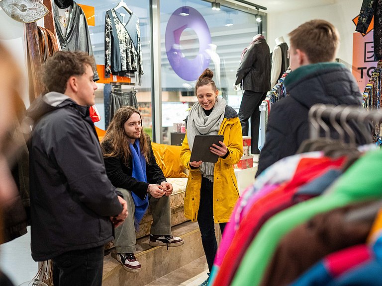 In einem Second Hand Modeladen in Stuttgart erläutert unser Guide Sabrina einer kleiner Gruppe die Vorteile von nachhaltiger Mode.