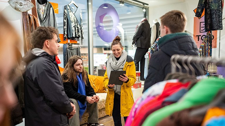 In einem Second Hand Modeladen in Stuttgart erläutert unser Guide Sabrina einer kleiner Gruppe die Vorteile von nachhaltiger Mode.