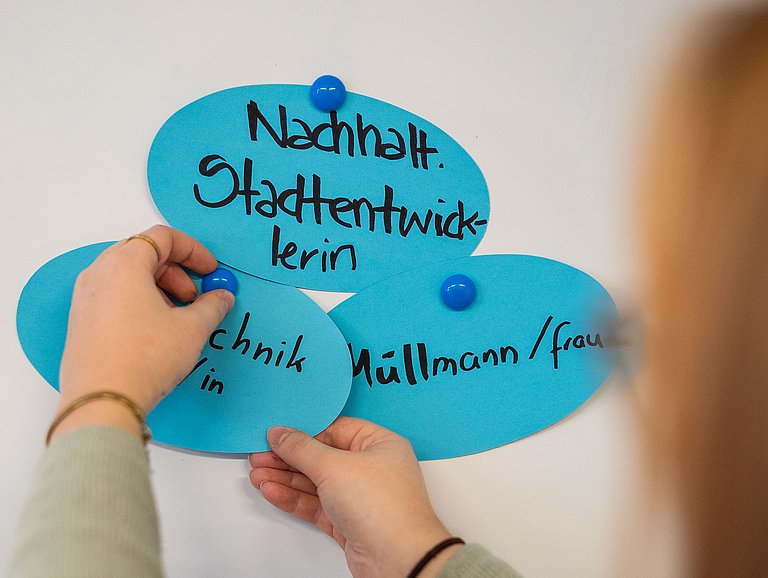 Junge Frau pinnt verschiedene Berufe an eine Pinnwand