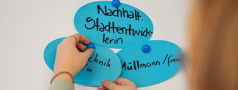 Junge Frau pinnt verschiedene Berufe an eine Pinnwand